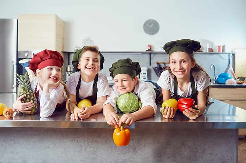 Funny children in the uniform of cooks on the table in vegetable